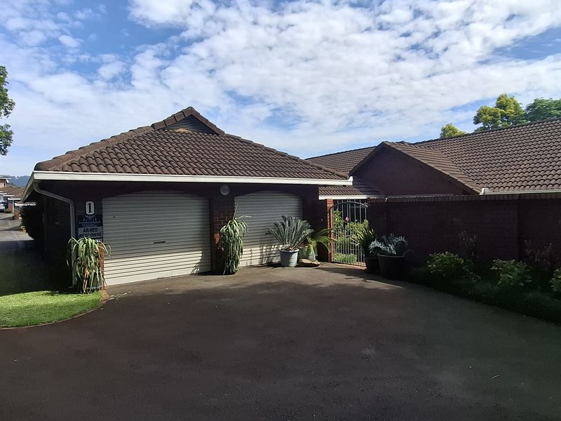 Front view of a townhouse featuring a double garage with roller doors, brick exterior, and a paved driveway.