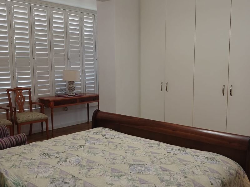 A well-maintained bedroom featuring built-in cupboards, plantation shutters, and crown molding, providing a clean and functional living space.