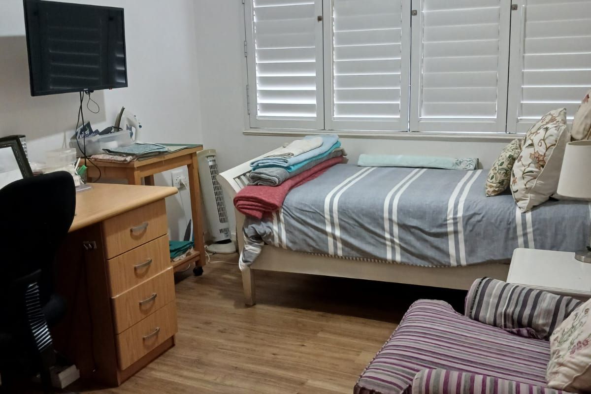 A functional bedroom featuring laminate flooring, white plantation shutters, and coving detail, providing a neutral base for potential interior updates.