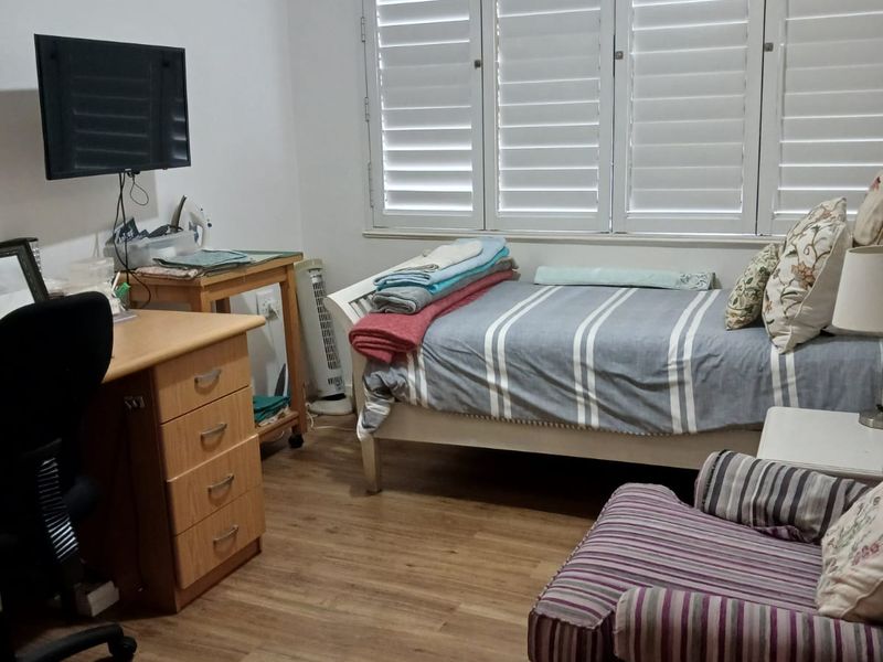 A functional bedroom featuring laminate flooring, white plantation shutters, and coving detail, providing a neutral base for potential interior updates.
