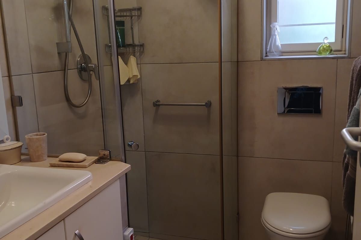 A functional bathroom featuring a glass-enclosed shower, wall-mounted toilet with concealed cistern, vanity cabinet with basin, and neutral wall and floor tiling.