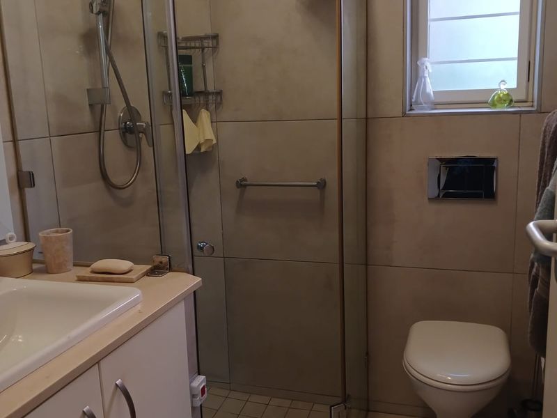 A functional bathroom featuring a glass-enclosed shower, wall-mounted toilet with concealed cistern, vanity cabinet with basin, and neutral wall and floor tiling.