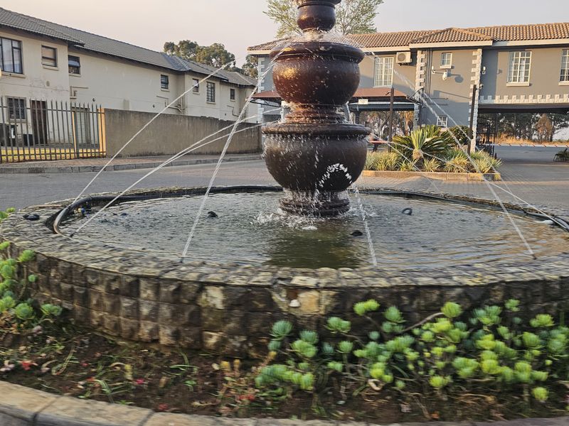 A well-maintained townhouse complex entrance featuring a central stone water fountain and paved driveway access.