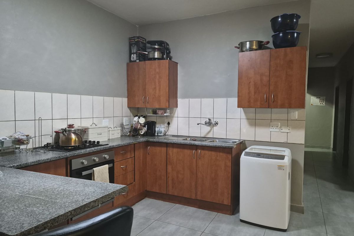 Functional kitchen featuring wood-finish cabinetry, granite countertops, a gas hob, built-in oven, and tiled backsplash with neutral floor tiling.
