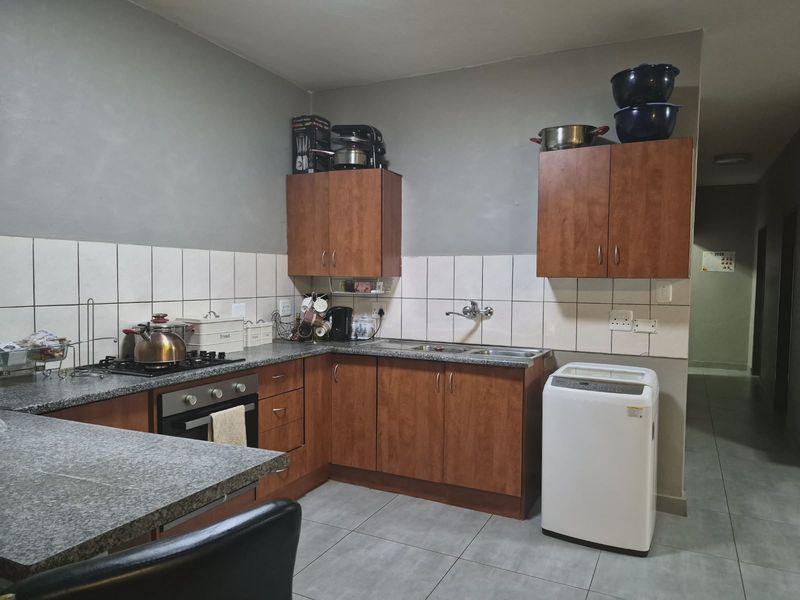 Functional kitchen featuring wood-finish cabinetry, granite countertops, a gas hob, built-in oven, and tiled backsplash with neutral floor tiling.