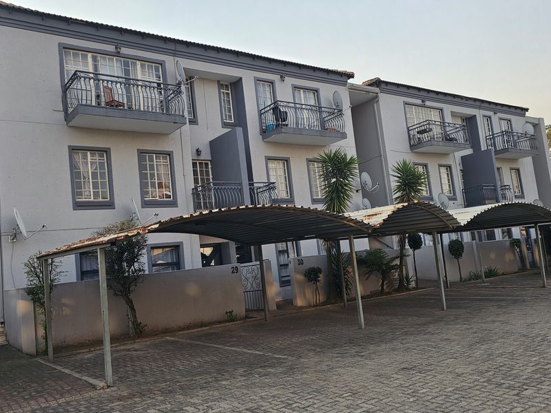 Front elevation of a multi-story townhouse complex featuring covered parking carports, private balconies with iron railings, and paved driveway access.