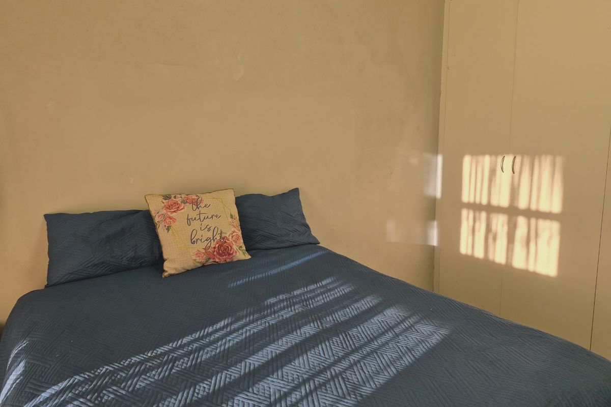 A bedroom featuring a built-in wardrobe with neutral wall finishes and natural light casting shadows across the space.