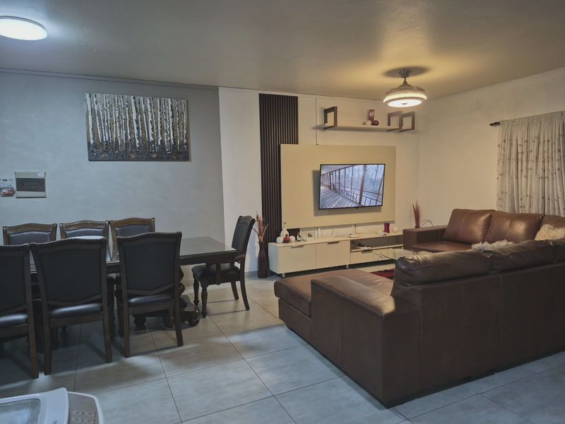 Open-plan living and dining area featuring tiled flooring, a modern media wall with slatted accents, and a ceiling fan.