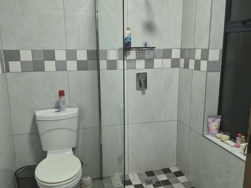 A modern bathroom featuring a walk-in shower with a glass screen, tiled walls, and a tiled floor with a decorative checkerboard accent.