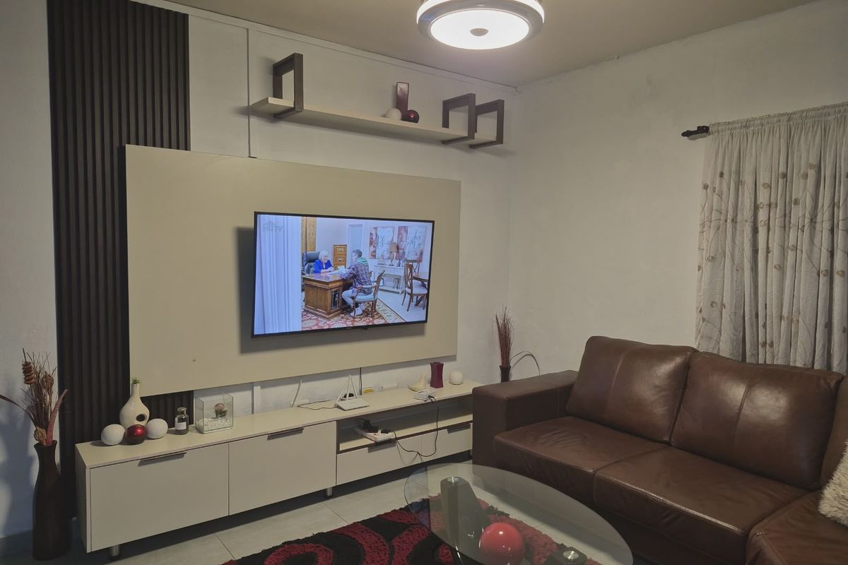 A well-maintained living room featuring a modern built-in media console with integrated slatted wall paneling and a contemporary ceiling light fixture.