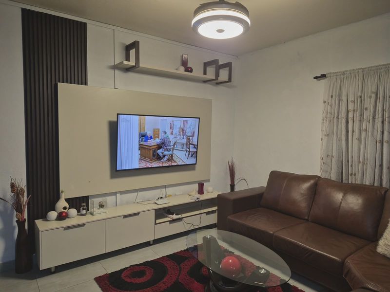 A well-maintained living room featuring a modern built-in media console with integrated slatted wall paneling and a contemporary ceiling light fixture.