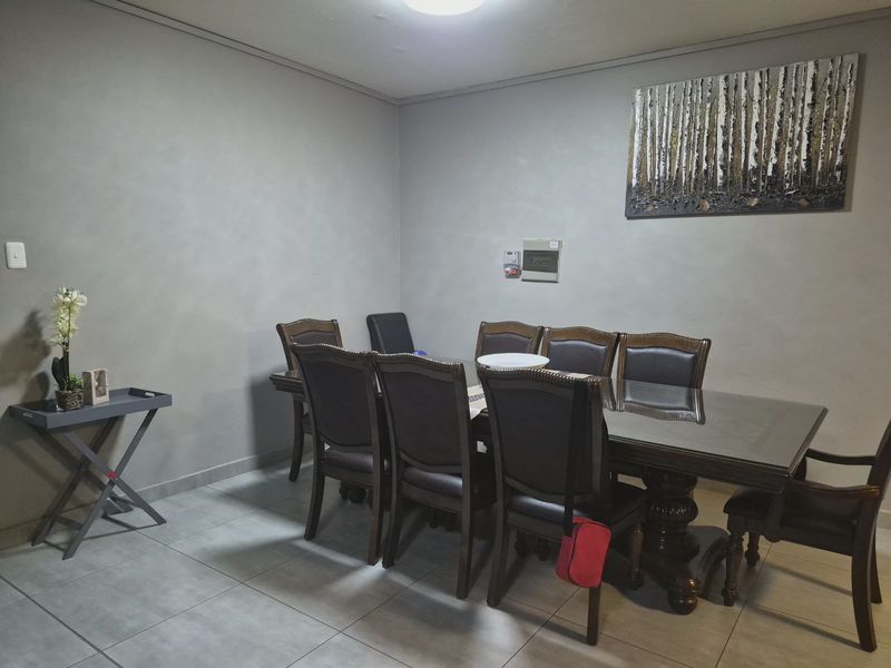 A functional dining room featuring neutral grey walls and large format floor tiles, providing a clean and versatile space for family meals.