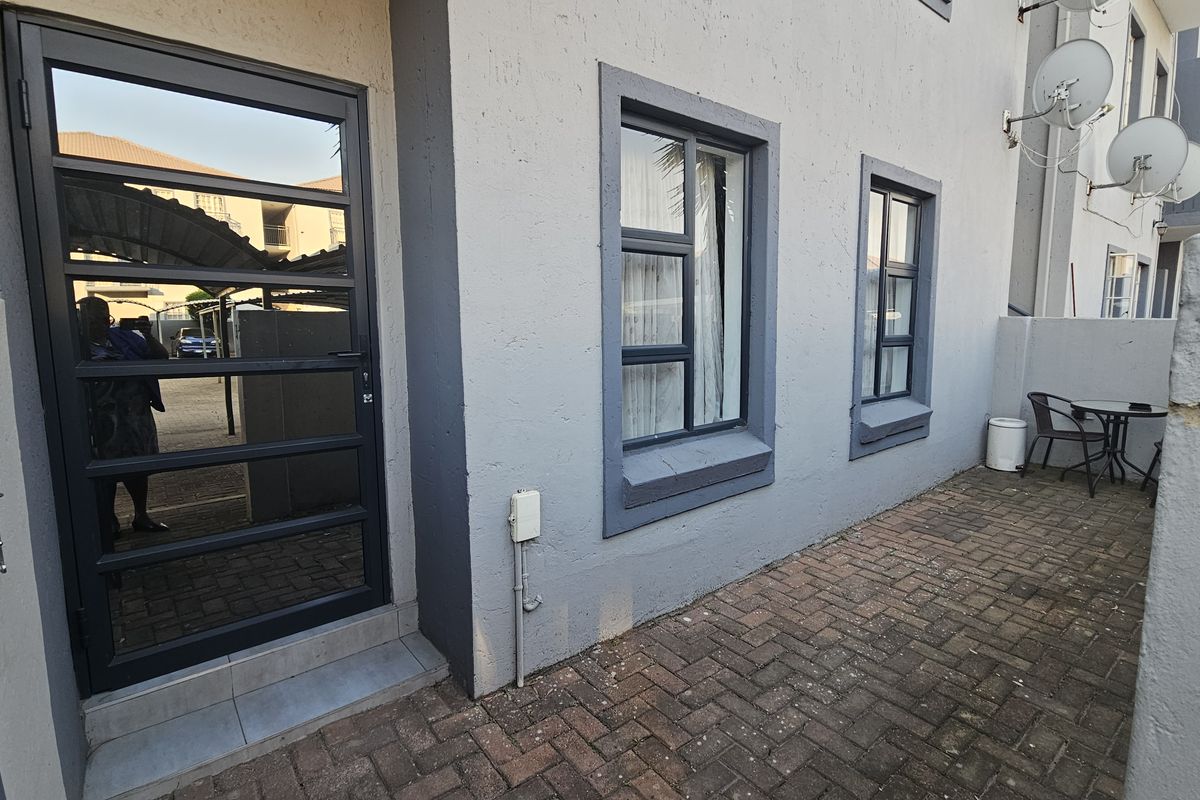A rear exterior view of the townhouse featuring a paved patio area, aluminium window frames, and a secure glass-panelled door.