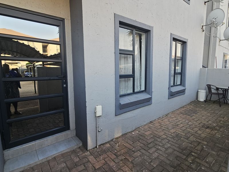 A rear exterior view of the townhouse featuring a paved patio area, aluminium window frames, and a secure glass-panelled door.