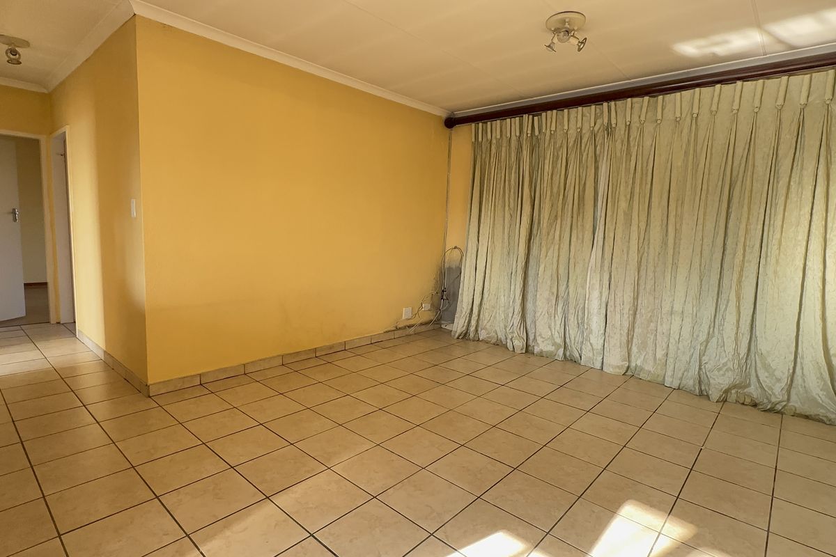 An empty living room featuring ceramic floor tiles, cove cornicing, and yellow painted walls, offering a blank canvas for potential interior updates.