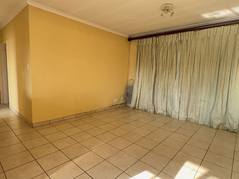 An empty living room featuring ceramic floor tiles, cove cornicing, and yellow painted walls, offering a blank canvas for potential interior updates.