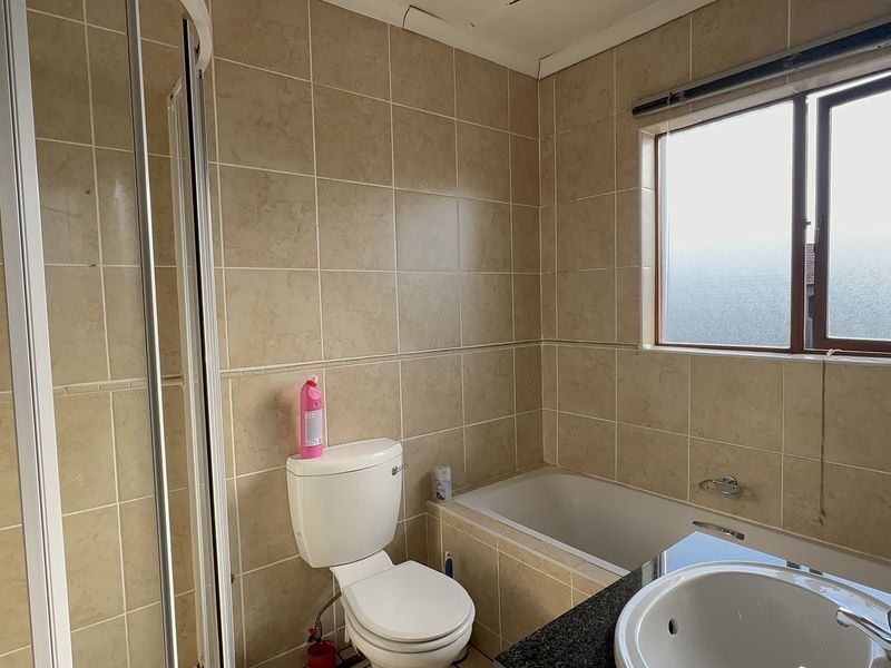 A functional bathroom featuring a shower enclosure, bathtub, vanity basin, and neutral wall tiling, offering a practical layout with natural light.