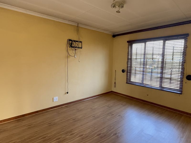An empty living room featuring laminate flooring, window blinds, and exposed wall wiring, offering a blank canvas for renovation and interior design updates.