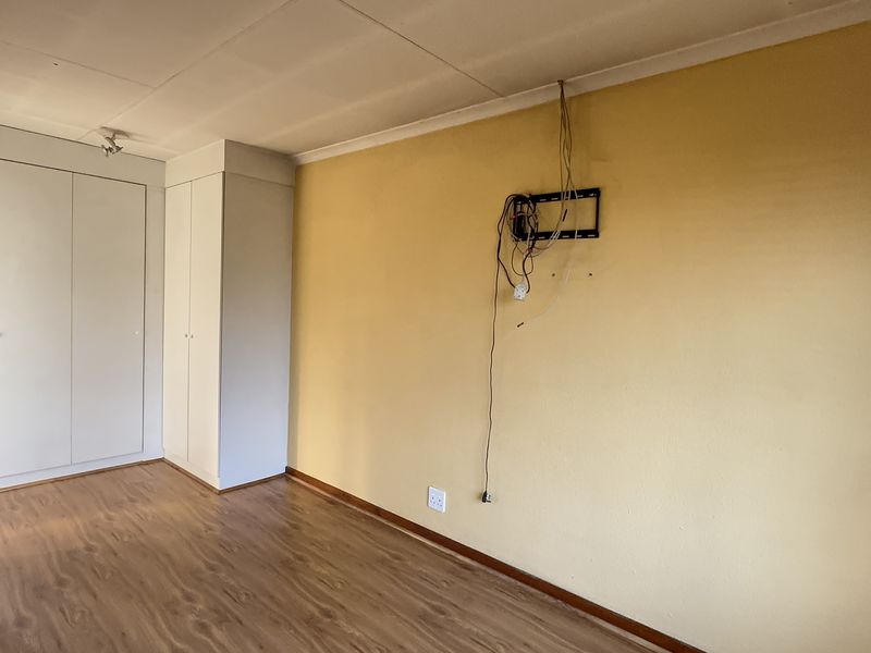 An empty bedroom featuring laminate flooring, built-in cupboards, and a yellow feature wall with exposed electrical wiring.