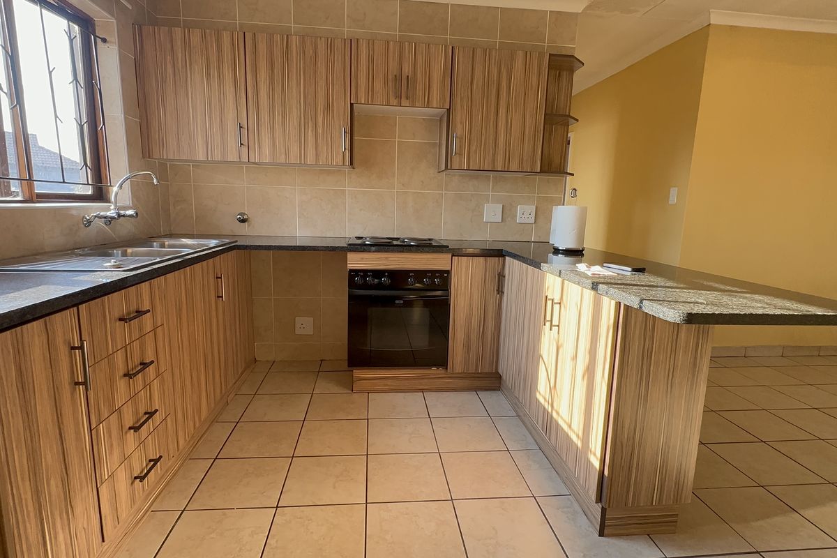 A functional kitchen featuring wood-look laminate cabinetry, granite countertops, a built-in oven with hob, and a convenient breakfast bar area.