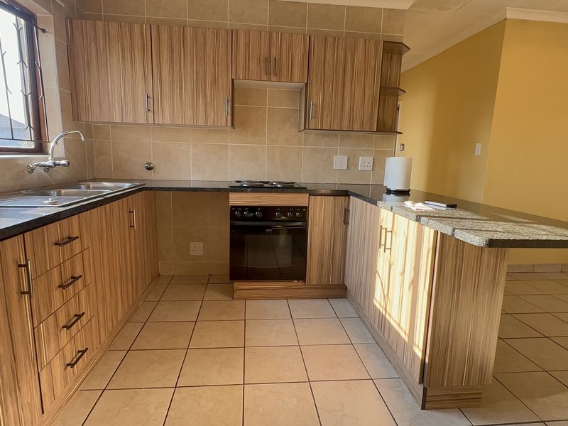 A functional kitchen featuring wood-look laminate cabinetry, granite countertops, a built-in oven with hob, and a convenient breakfast bar area.