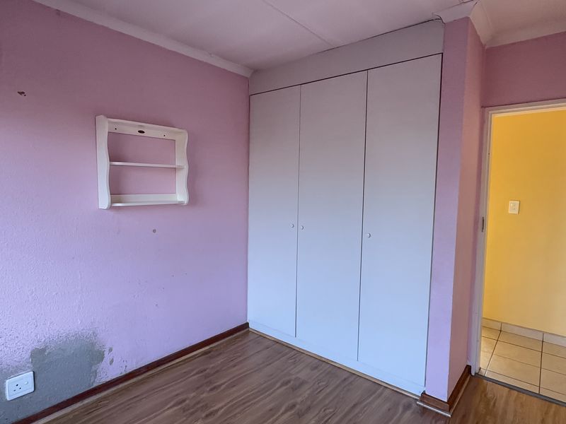 A vacant bedroom featuring built-in cupboards, laminate flooring, and visible wall surface damage requiring repair and repainting.