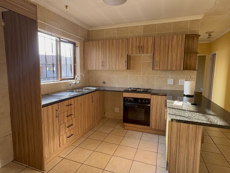 A functional kitchen featuring wood-finish cabinetry, granite countertops, built-in oven and hob, and tiled flooring, offering a practical layout for daily use.