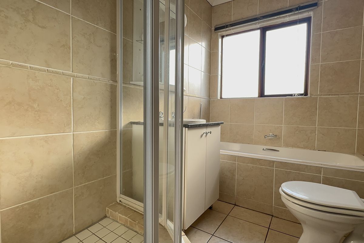 A functional bathroom featuring a separate shower enclosure, bathtub, vanity cabinet with basin, and neutral wall and floor tiling.