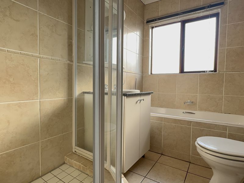 A functional bathroom featuring a separate shower enclosure, bathtub, vanity cabinet with basin, and neutral wall and floor tiling.