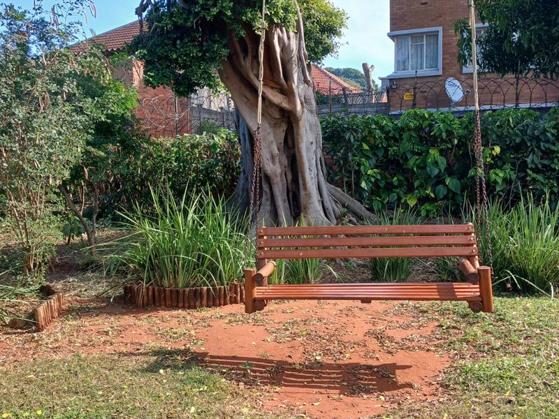 A communal garden area featuring a large mature tree and established landscaping, situated adjacent to an apartment building.