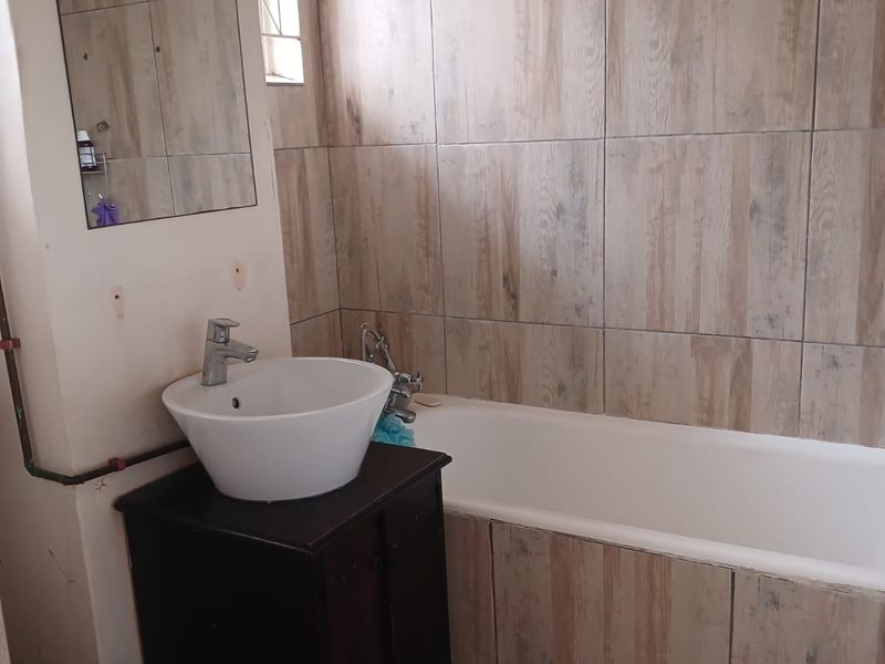 A functional bathroom featuring a vessel sink on a vanity cabinet, a bathtub with shower head, and wood-look wall tiling.