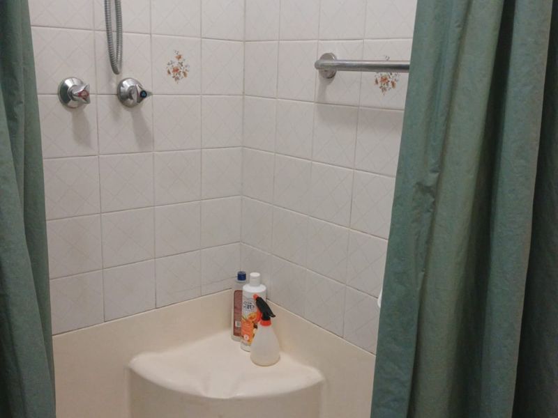 A functional shower enclosure featuring white wall tiles with decorative accents, a chrome shower mixer, and a built-in shower base with a grab rail.
