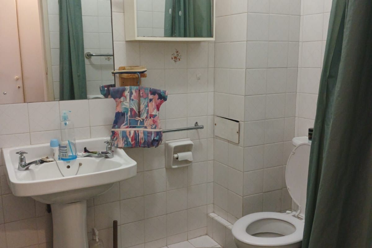 A functional bathroom featuring a pedestal basin, toilet, and wall-mounted medicine cabinet, finished with white wall tiles and green floor tiles.