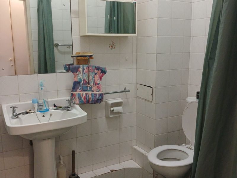 A functional bathroom featuring a pedestal basin, toilet, and wall-mounted medicine cabinet, finished with white wall tiles and green floor tiles.
