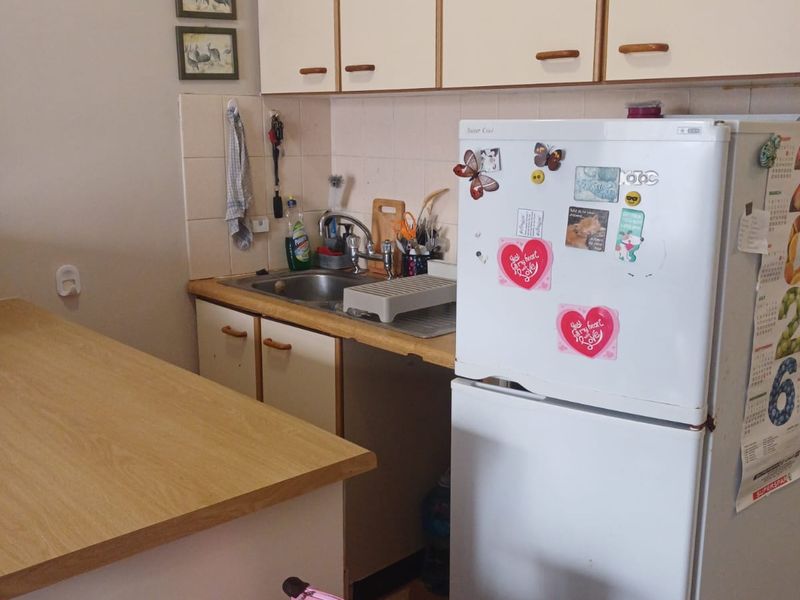 A compact kitchen featuring dated laminate countertops, built-in cabinetry, and a stainless steel sink with a tiled backsplash.
