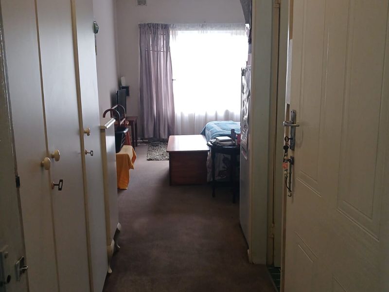A functional hallway featuring built-in storage cupboards and carpeted flooring, leading towards a bedroom area with natural light.