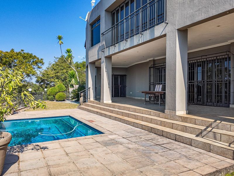 Spacious outdoor entertainment area featuring a swimming pool, tiled patio, and a covered balcony with metal railings overlooking the garden.
