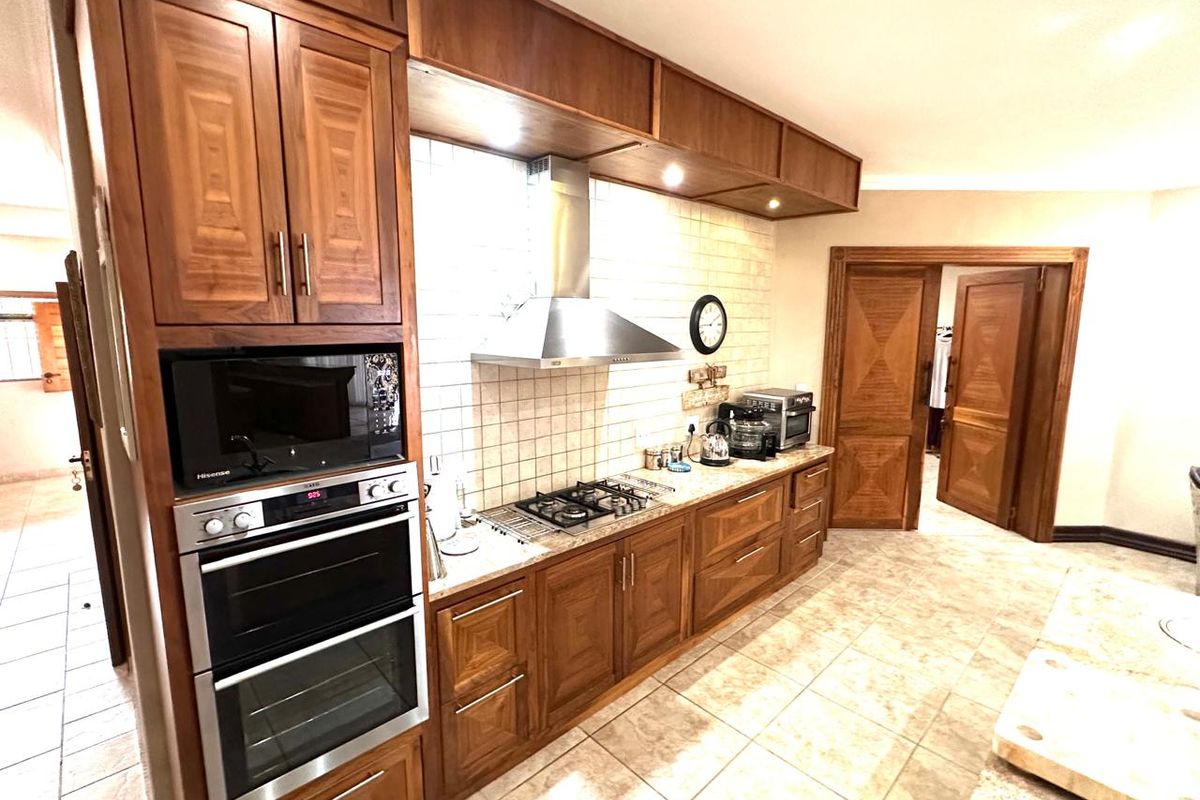 A well-maintained kitchen featuring warm-toned wooden cabinetry, a built-in double oven, gas hob with extractor fan, and classic tiled finishes.