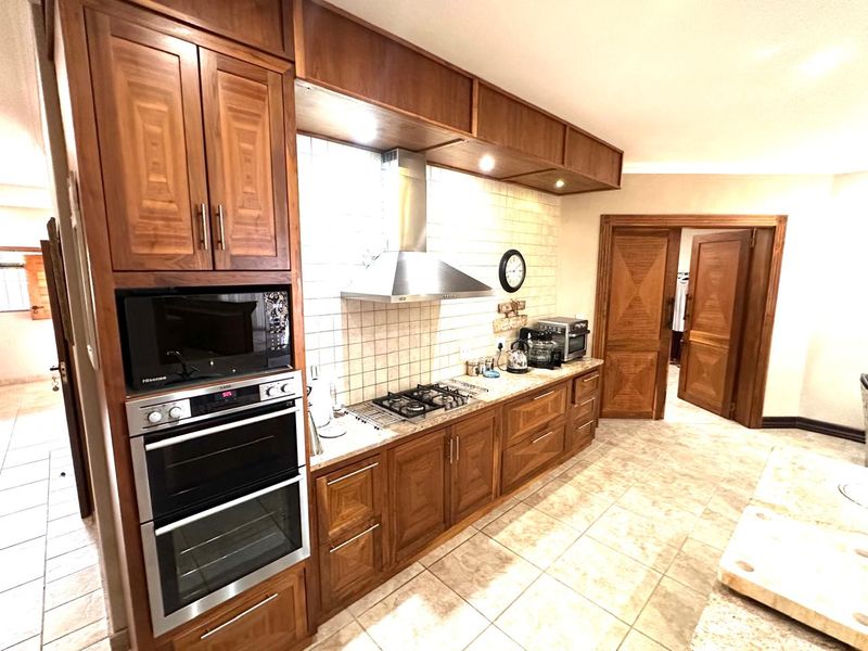 A well-maintained kitchen featuring warm-toned wooden cabinetry, a built-in double oven, gas hob with extractor fan, and classic tiled finishes.