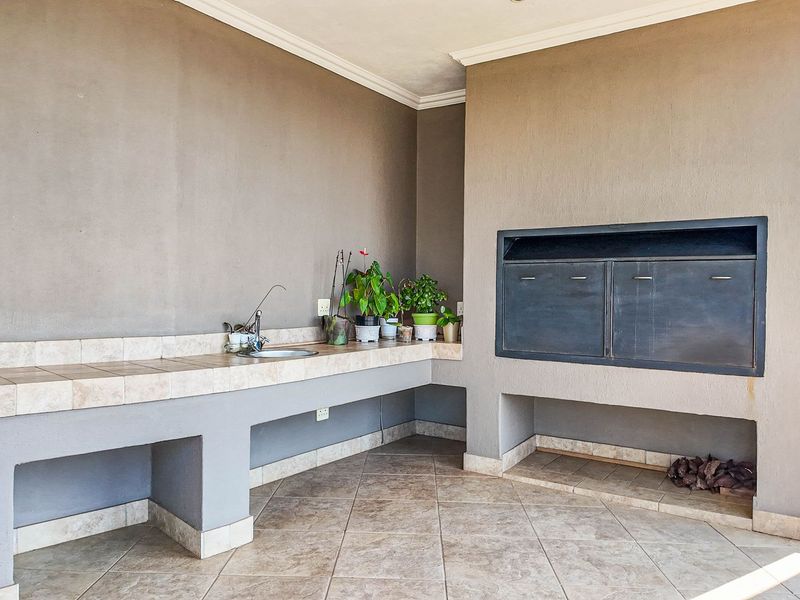 Covered patio area featuring a built-in braai, tiled countertop with integrated sink, and durable tiled flooring, ideal for outdoor entertaining.
