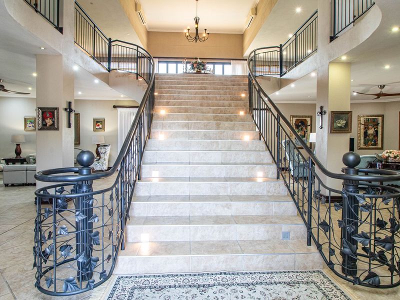 A grand entrance hall featuring a central tiled staircase with decorative wrought iron balustrades and open-plan living areas on either side.