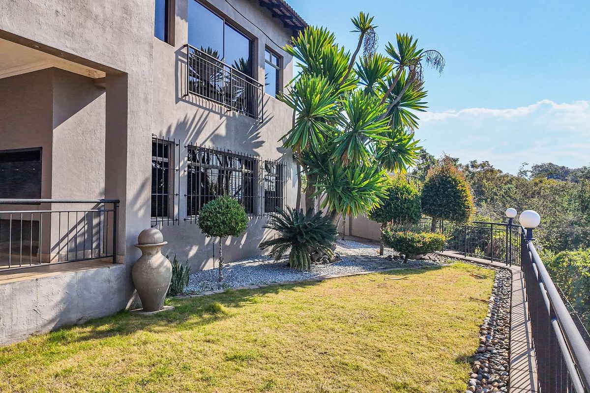Rear exterior view of the property featuring a covered patio, landscaped garden area with stone accents, and secure metal railings overlooking the surrounding landscape.