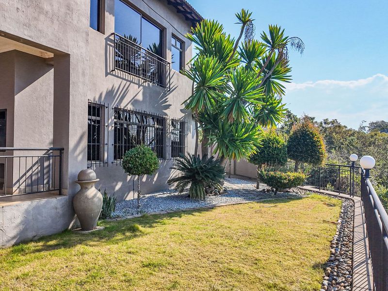 Rear exterior view of the property featuring a covered patio, landscaped garden area with stone accents, and secure metal railings overlooking the surrounding landscape.