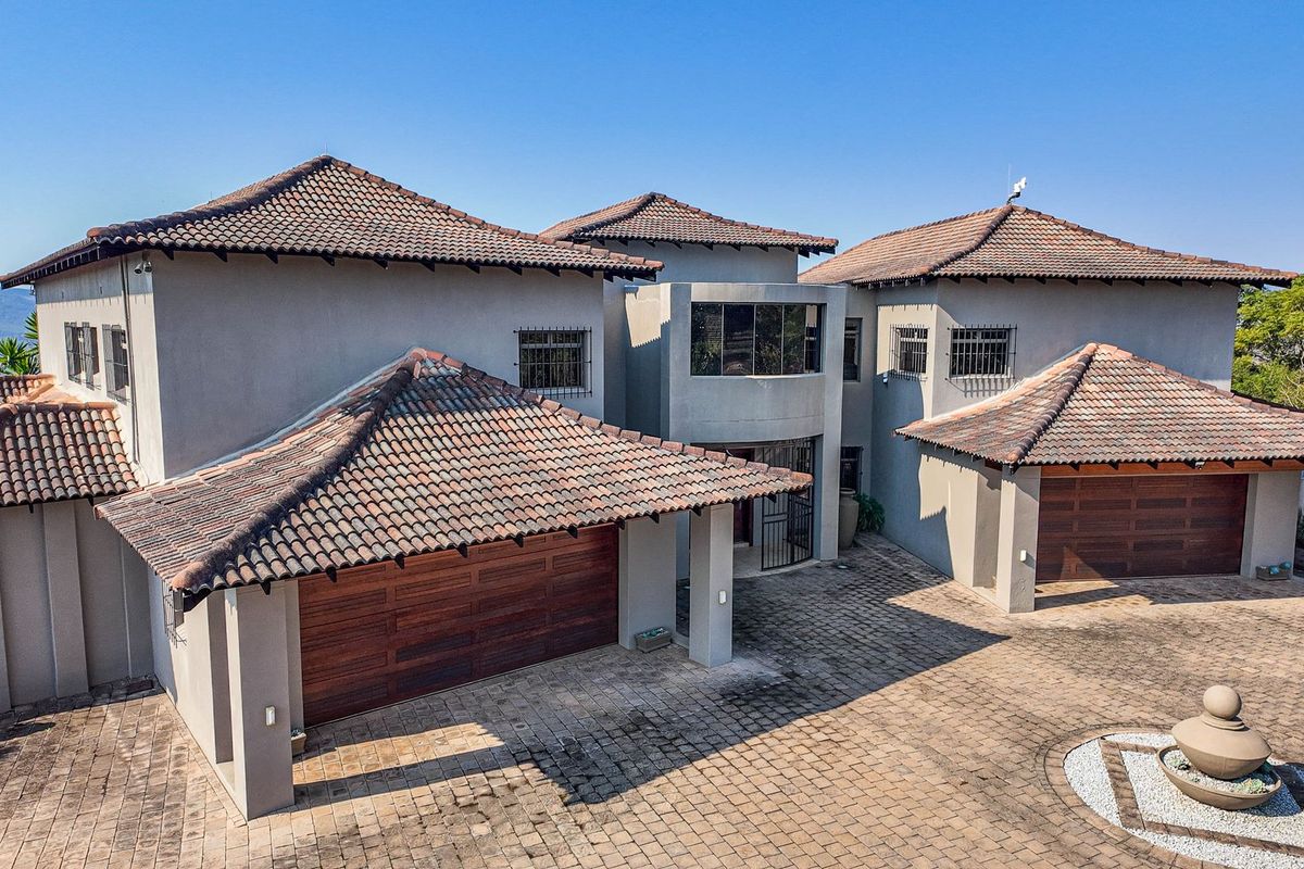 Aerial view of a large farm residence featuring a multi-pitched tiled roof, extensive paved driveway, and double garage configuration.