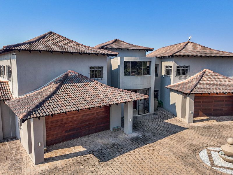 Aerial view of a large farm residence featuring a multi-pitched tiled roof, extensive paved driveway, and double garage configuration.