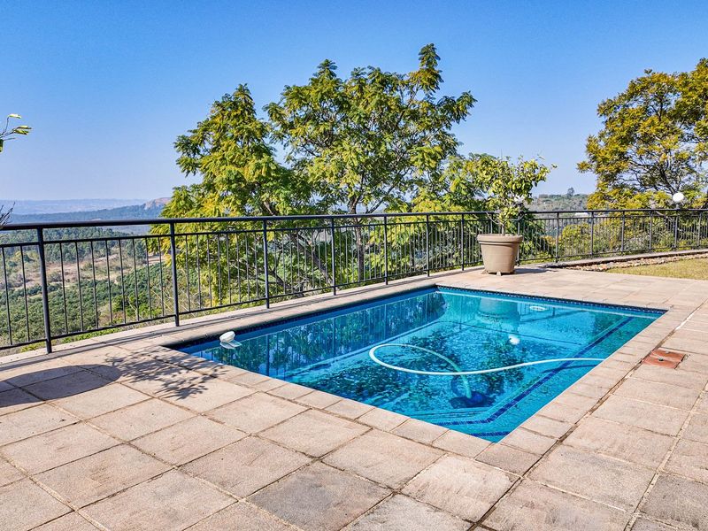 A well-maintained swimming pool area featuring a paved deck and metal safety railing, offering expansive views of the surrounding landscape.