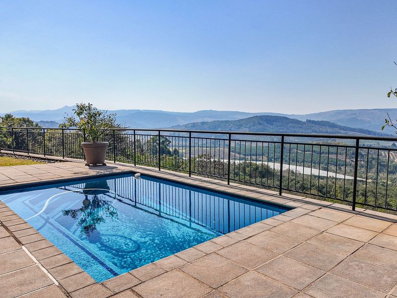 A well-maintained swimming pool area featuring a tiled deck and metal balustrade, offering expansive scenic views of the surrounding landscape.