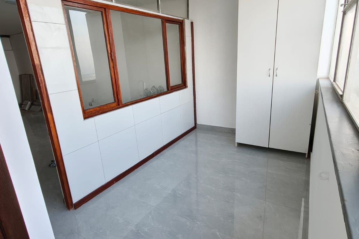 A bright, empty bedroom featuring modern grey tiled flooring, a built-in wardrobe, and a unique timber-framed internal window partition.