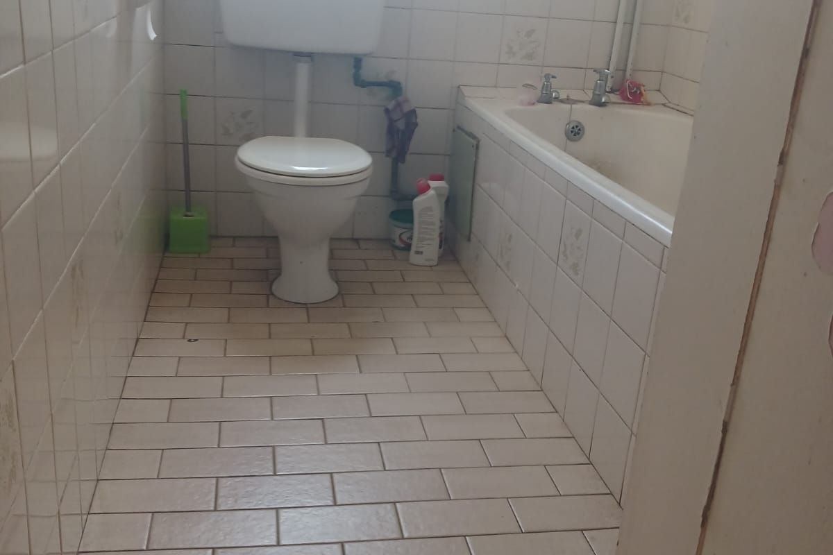 A functional bathroom featuring a standard bathtub, toilet, and tiled finishes throughout, offering potential for modernization and cosmetic updates.