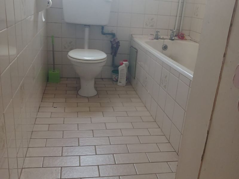 A functional bathroom featuring a standard bathtub, toilet, and tiled finishes throughout, offering potential for modernization and cosmetic updates.